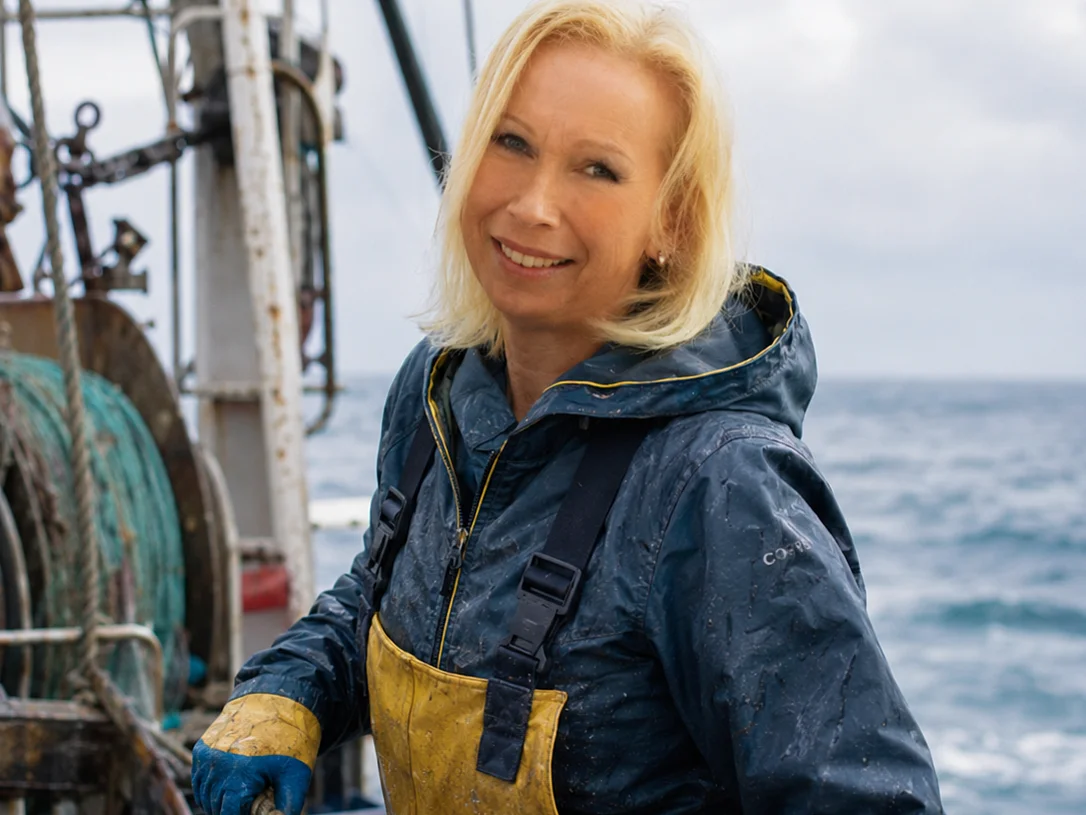Junge blonde Frau auf Fischkutter mit Fischen in Kisten