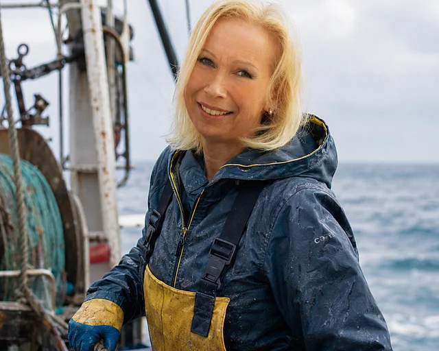 Junge blonde Frau auf Fischkutter mit Fischen in Kisten